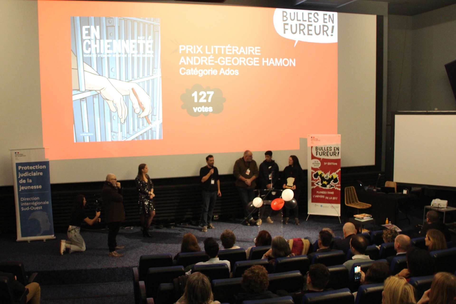 Présentation par les organisateurs et organisatrices de la BD gagnante du prix Bulles en fureur "En chienneté" dans la catégorie Ados sur un écran projeté dans un amphithéâtre lors de la 31e édition le 8 février 2024 à Angoulême.